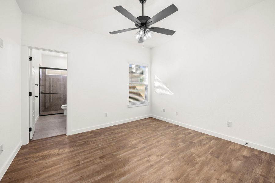 A well-lit bedroom with rich wood flooring offers direct access to a private bathroom.
