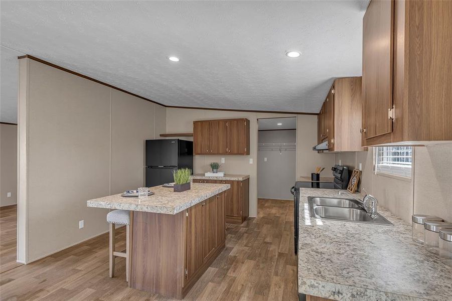 Kitchen featuring light hardwood / wood-style flooring, a center island, black fridge, lofted ceiling, and sink