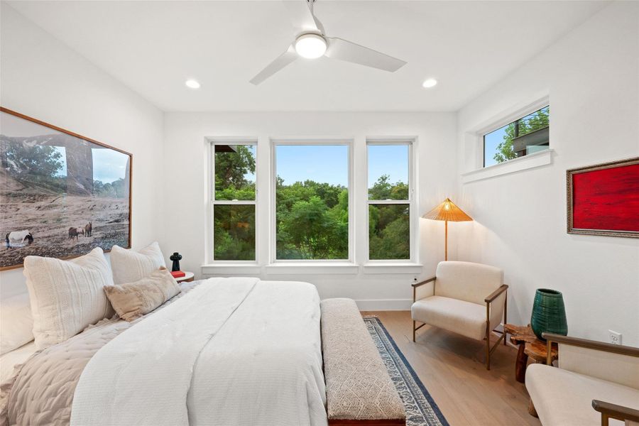 A tranquil primary bedroom suite showcases tree-filled outdoor views and light wood flooring. A tranquil primary bedroom suite showcases tree-filled outdoor views and light wood flooring.