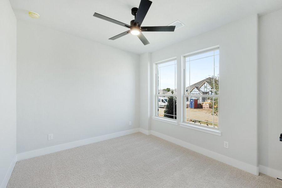 Empty bedroom with carpet flooring, black ceiling fan, and two windows with neighborhood view