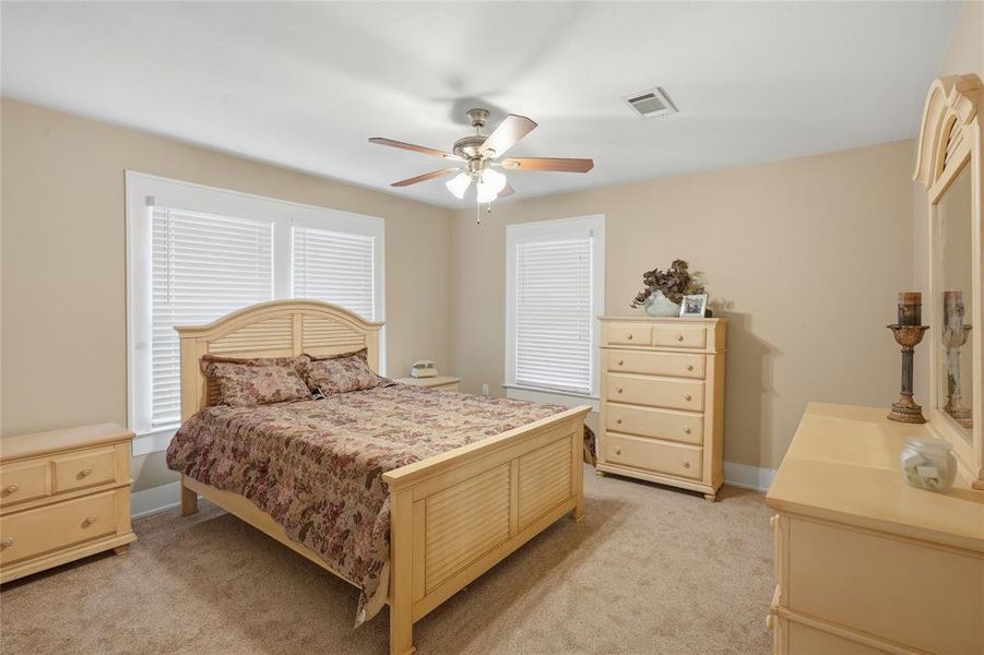 Carpeted bedroom featuring two windows with blinds, a ceiling fan with integrated lighting, and neutral wall tones
