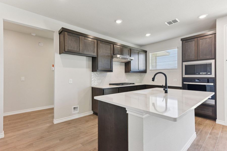Kitchen featuring dark brown cabinetry, light wood-style flooring, light stone counters, and recessed lighting
