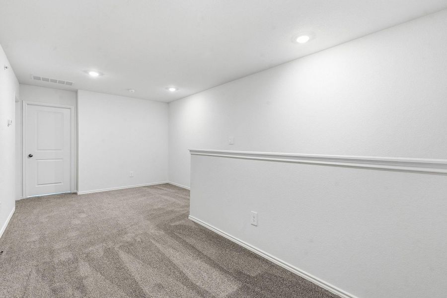 Carpeted room featuring recessed lighting, a white painted door, and a half-wall with chair rail molding Carpeted room featuring recessed lighting, a white painted door, and a half-wall with chair rail molding