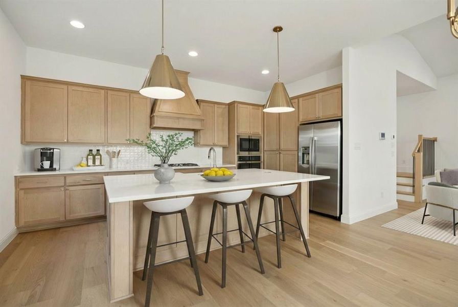 Kitchen with a kitchen breakfast bar, decorative light fixtures, a kitchen island with sink, stainless steel appliances, and light wood-style floors Kitchen with a kitchen breakfast bar, decorative light fixtures, a kitchen island with sink, stainless steel appliances, and light wood-style floors