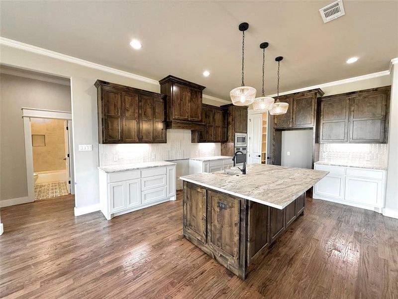 Kitchen featuring dark brown cabinets, decorative backsplash, an island with sink, light stone counters, and a kitchen bar Kitchen featuring dark brown cabinets, decorative backsplash, an island with sink, light stone counters, and a kitchen bar