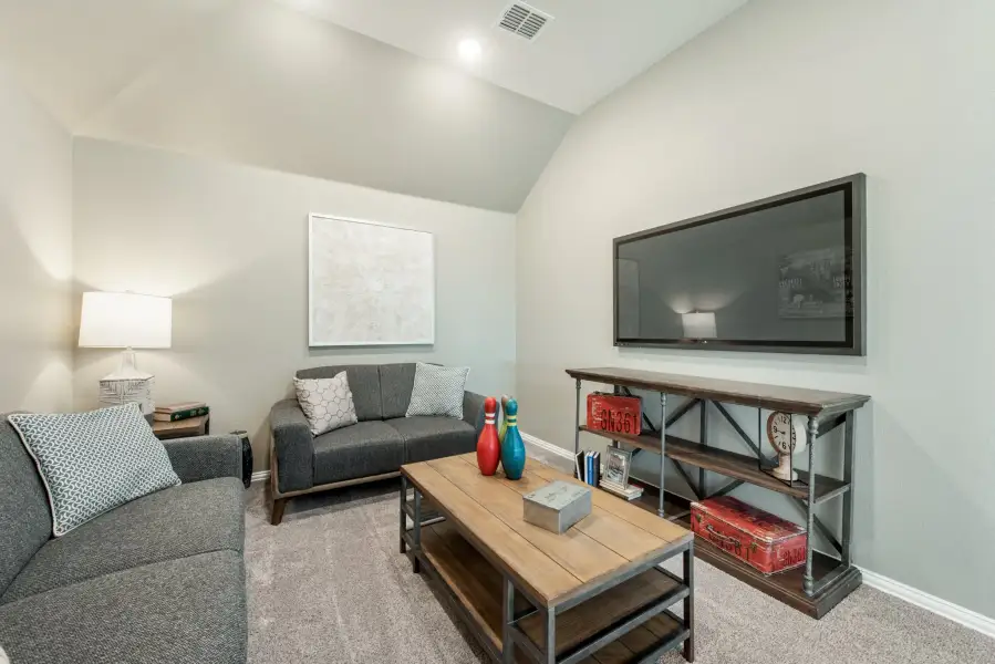 Living room with vaulted ceiling, gray sofas, wood coffee table, and wall-mounted TV on carpet flooring