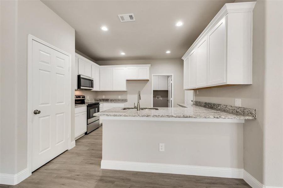 Kitchen featuring white cabinetry, kitchen peninsula, stainless steel appliances, light hardwood / wood-style flooring, and sink