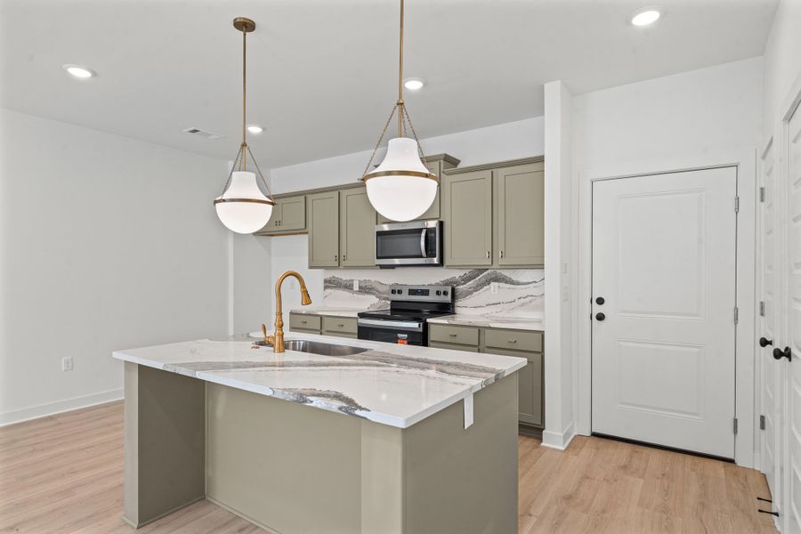 Kitchen featuring a central island with a sink, white countertops, a brass-finish faucet, and two pendant lights