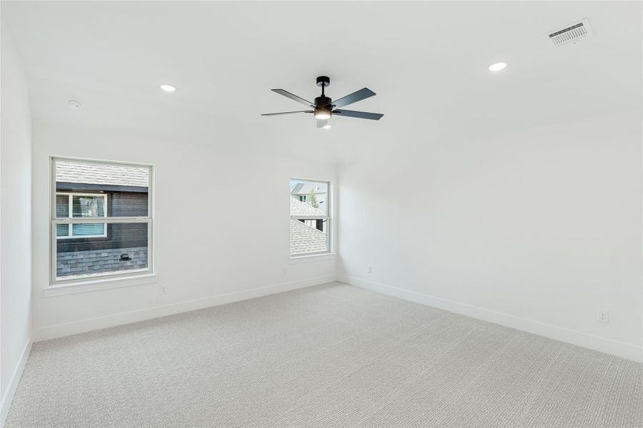 Empty bedroom with white walls, carpet flooring, ceiling fan, and two windows