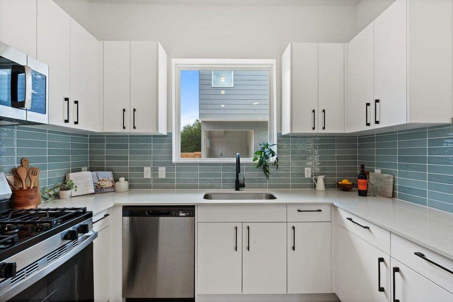 The kitchen features white cabinetry with black hardware, a light-colored countertop, and a blue subway tile backsplash