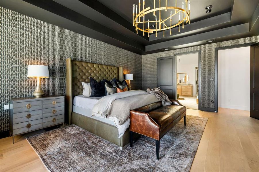 Bedroom featuring a raised ceiling, wallpapered walls, a chandelier, light wood-style floors, and ensuite bathroom Bedroom featuring a raised ceiling, wallpapered walls, a chandelier, light wood-style floors, and ensuite bathroom