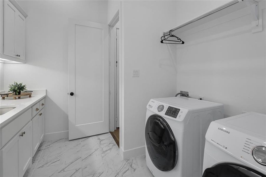Laundry room featuring light-toned cabinetry with dark hardware, a white countertop with an undermount sink, and a clothes hanging rod