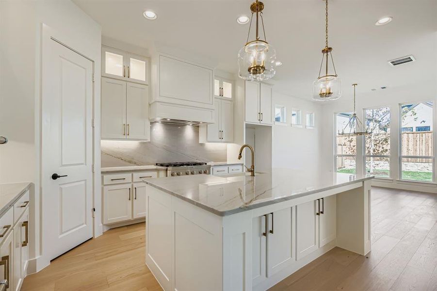 Kitchen featuring a chandelier, light wood-style flooring, tasteful backsplash, light stone countertops, and a center island with sink Kitchen featuring a chandelier, light wood-style flooring, tasteful backsplash, light stone countertops, and a center island with sink