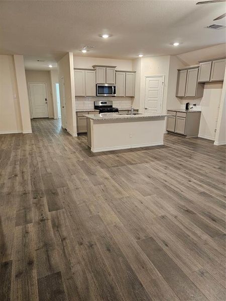 Kitchen with gray cabinets, range, hardwood / wood-style flooring, and a center island with sink