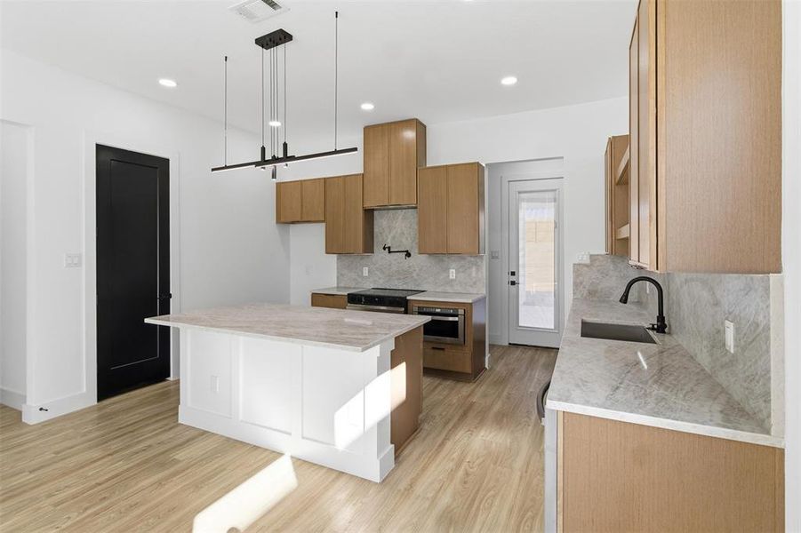 Kitchen featuring light stone countertops, a kitchen island, light wood-style floors, tasteful backsplash, and decorative light fixtures