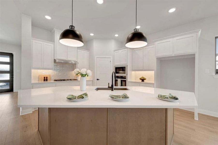 Two tone kitchen featuring light wood-style floors, a kitchen island with sink, oven, decorative backsplash, and two tone cabinets