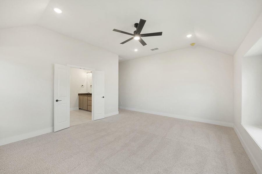Empty bedroom with carpet, ceiling fan, and open door leading to ensuite bathroom with vanity