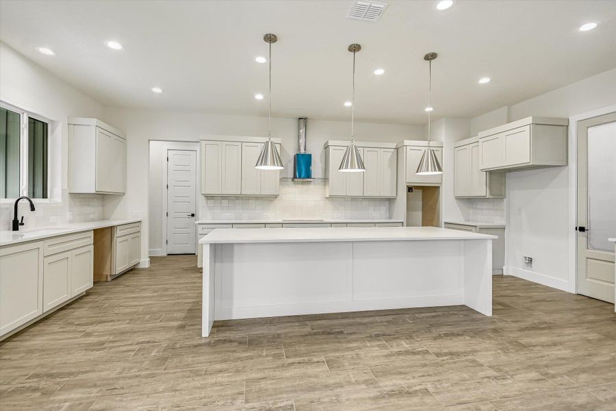 Kitchen with pendant lighting, a large island, decorative backsplash, and light stone countertops