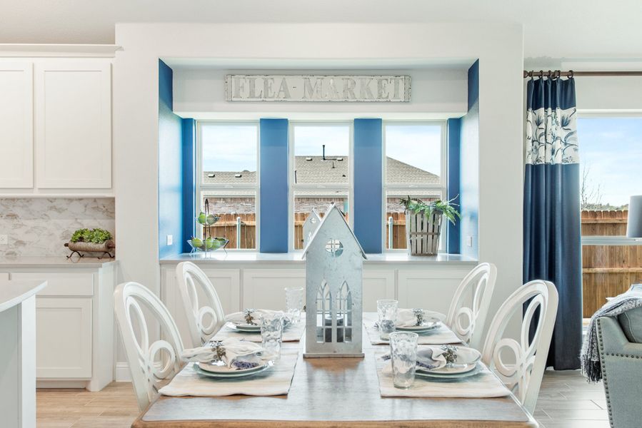 Dining area with set table, white chairs, blue accent wall, and large windows overlooking backyard