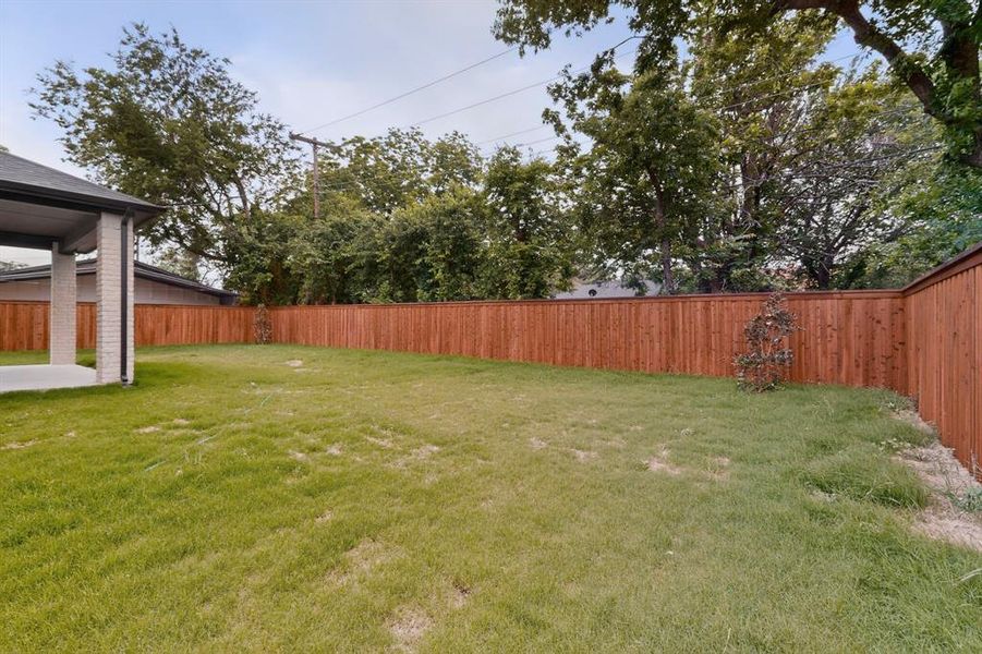 Expansive backyard featuring a new wood privacy fence, concrete patio, and lush green lawn