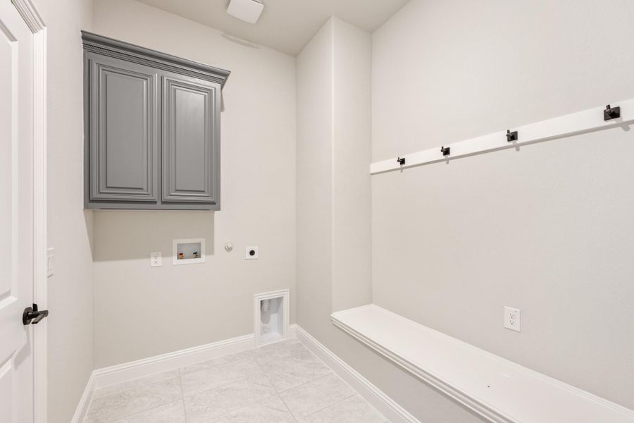 Mudroom and laundry room with gray upper cabinet, white bench, coat hooks, and washer hookups on tile floor Mudroom and laundry room with gray upper cabinet, white bench, coat hooks, and washer hookups on tile floor