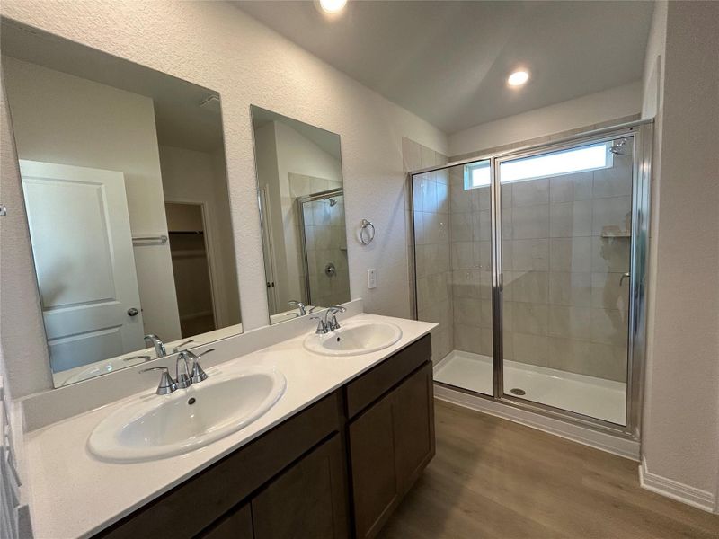 Bathroom featuring a textured wall, a shower stall, dark wood-type flooring, double vanity, and a walk in closet