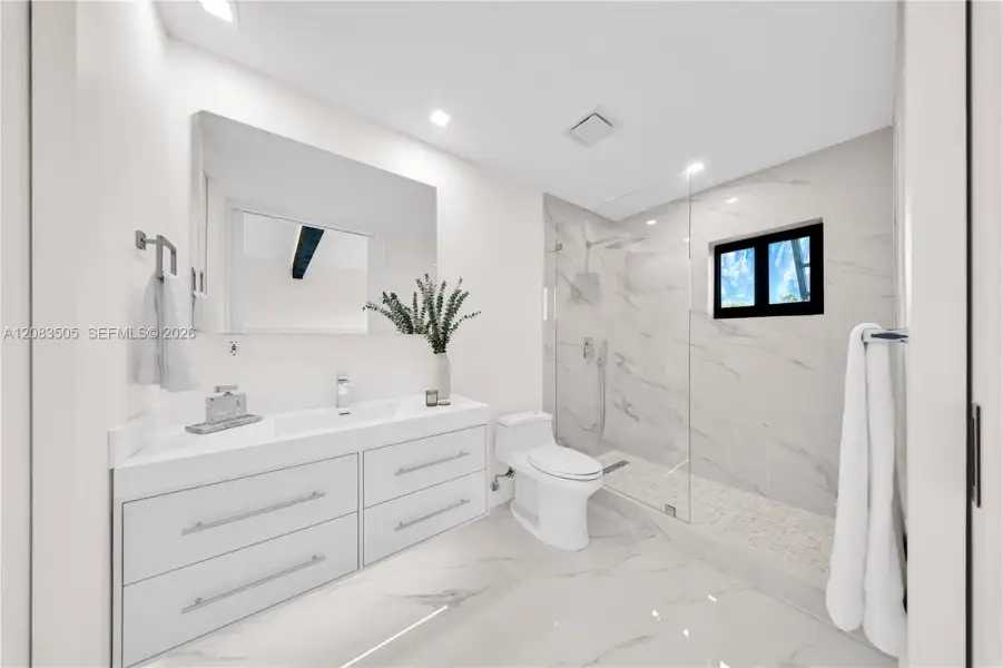 Bathroom featuring a white floating dual-drawer vanity with an integrated sink, floor-to-ceiling stone-style tile shower surround with a glass enclosure, and stone-style flooring Bathroom featuring a white floating dual-drawer vanity with an integrated sink, floor-to-ceiling stone-style tile shower surround with a glass enclosure, and stone-style flooring