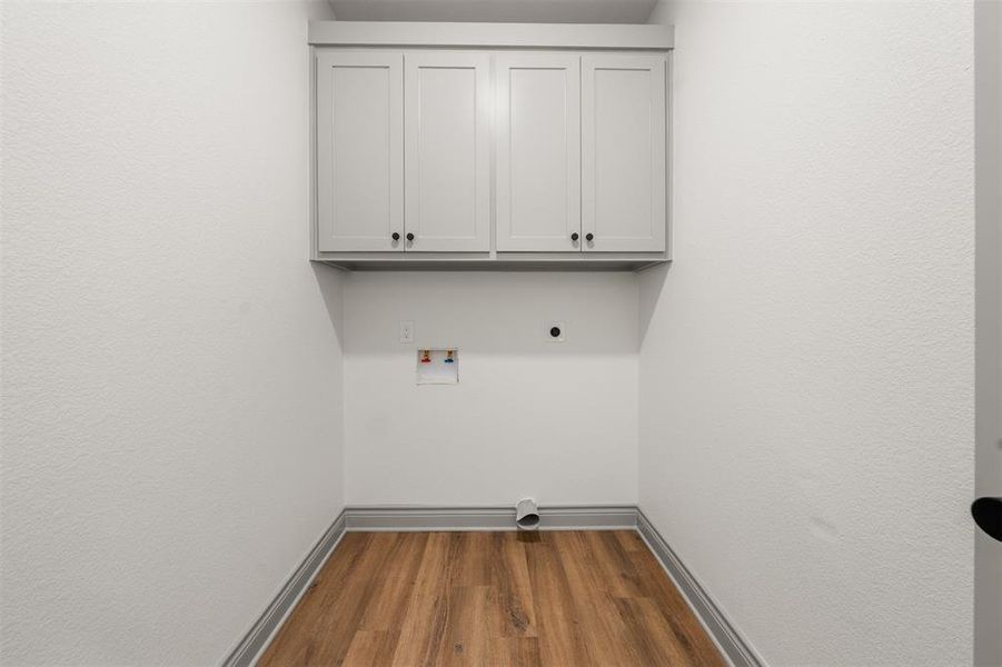 Laundry room featuring wood finished floors, hookup for a washing machine, cabinet space, and electric dryer hookup