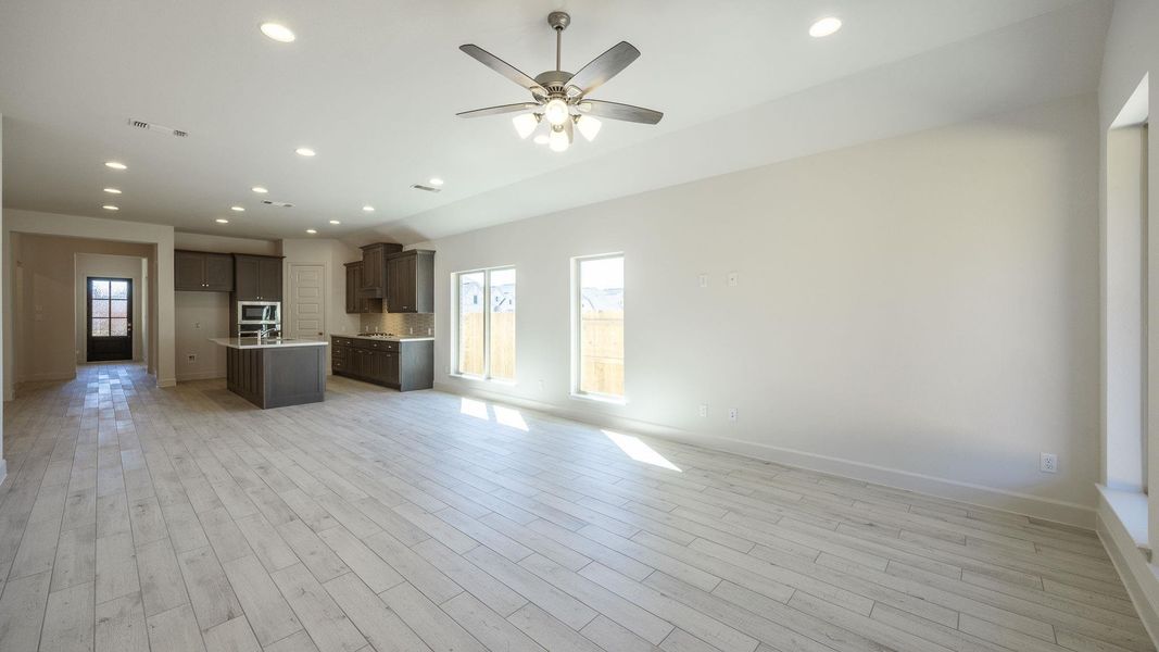 Unfurnished living room featuring a ceiling fan, light wood-style flooring, a healthy amount of sunlight, and visible vents