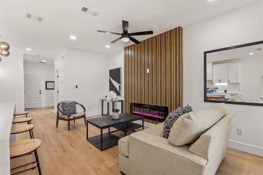 Living room featuring a glass covered fireplace, light wood finished floors, a ceiling fan, and recessed lighting