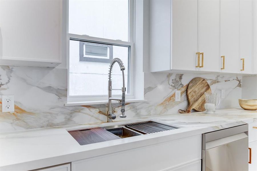 The sink area features a large window to let in natural lighting. There is a deep sink and stainless steel dishwasher.