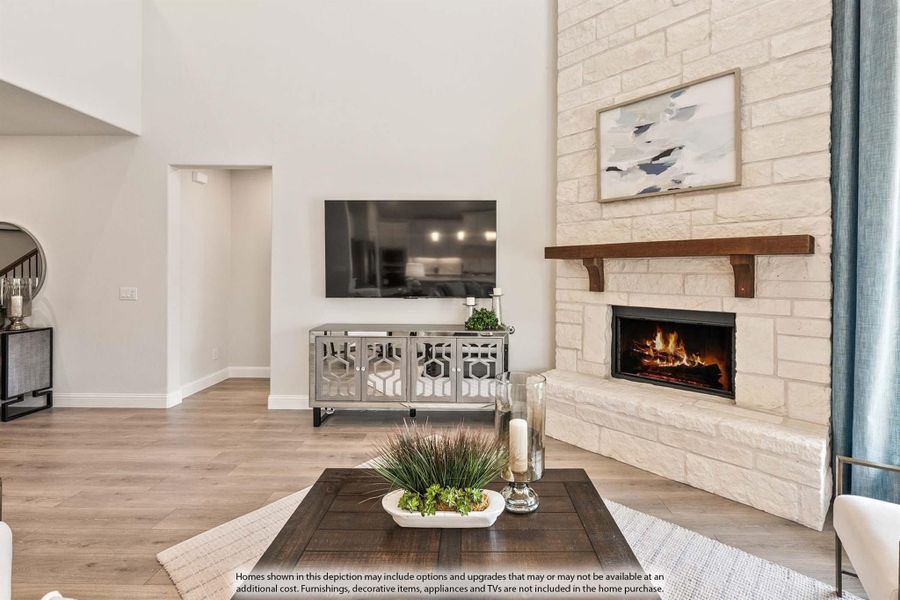 Living room with tall stone fireplace, wood mantel, high ceilings, and light hardwood floors