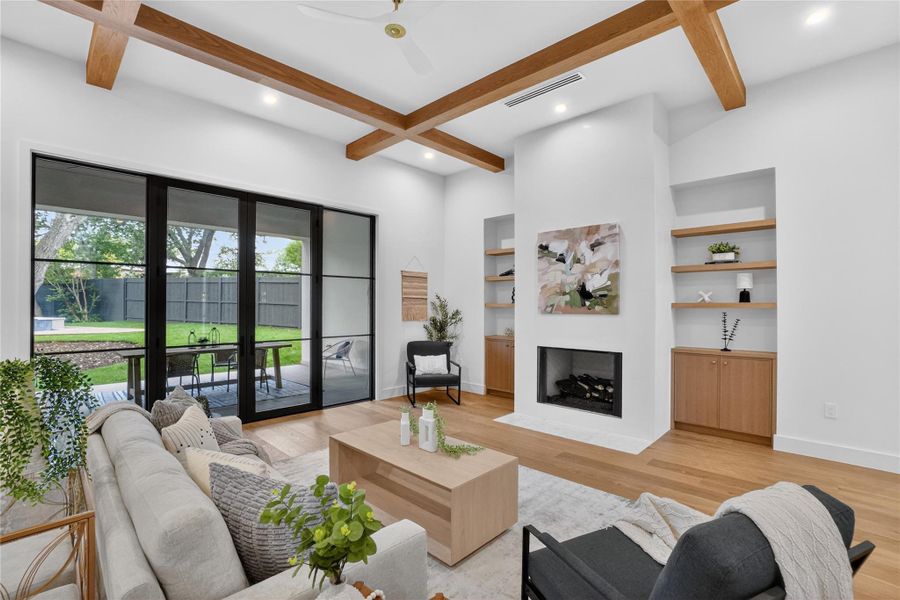 Exposed wood beams adorn the high ceilings of this elegant living room, boasting an integrated fireplace and seamless patio access.