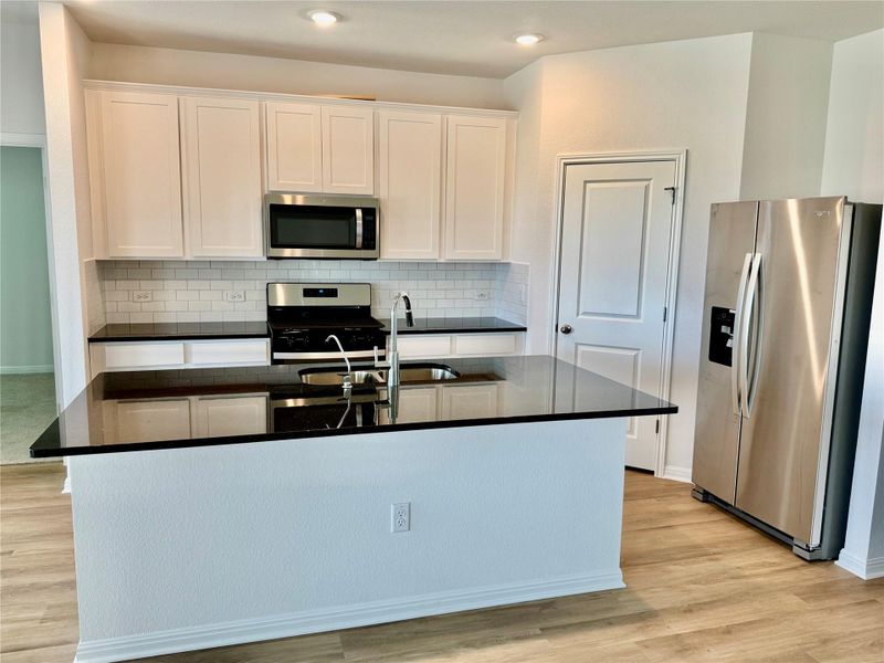 Kitchen featuring stainless steel appliances, tasteful backsplash, white cabinets, dark stone countertops, and light wood-style floors