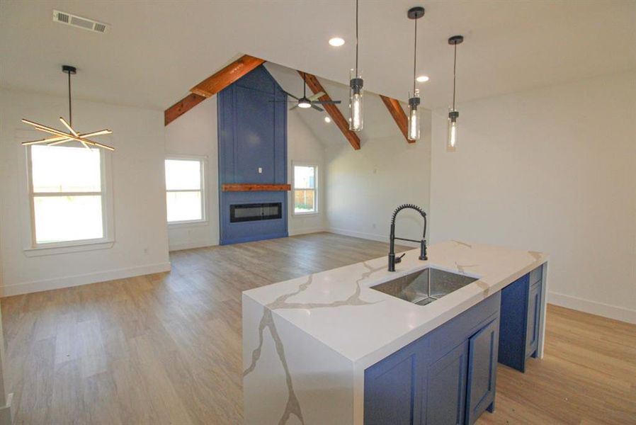 Kitchen featuring blue cabinets, light wood-style flooring, a fireplace, pendant lighting, and beam ceiling Kitchen featuring blue cabinets, light wood-style flooring, a fireplace, pendant lighting, and beam ceiling