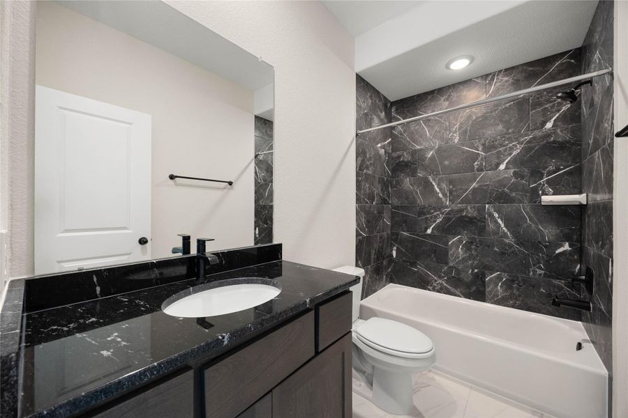 Luxurious full ensuite bathroom servicing the adjacent secondary bedroom with upscale finishes. This striking space features a deep bathtub/shower combination wrapped in dramatic, floor-to-ceiling dark marble-patterned tile. The matching espresso-toned vanity is paired with high-contrast black granite countertops, an undermount sink, and contemporary matte black plumbing fixtures that seamlessly tie the modern design together. Luxurious full ensuite bathroom servicing the adjacent secondary bedroom with upscale finishes. This striking space features a deep bathtub/shower combination wrapped in dramatic, floor-to-ceiling dark marble-patterned tile. The matching espresso-toned vanity is paired with high-contrast black granite countertops, an undermount sink, and contemporary matte black plumbing fixtures that seamlessly tie the modern design together.
