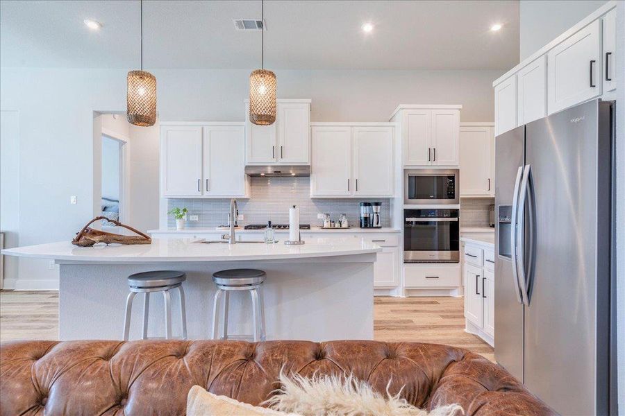 Kitchen featuring stainless steel appliances, light wood-style floors, a center island with sink, tasteful backsplash, and a kitchen bar Kitchen featuring stainless steel appliances, light wood-style floors, a center island with sink, tasteful backsplash, and a kitchen bar