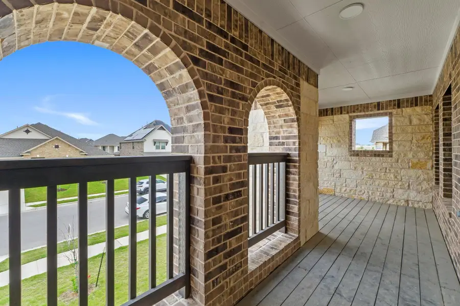 Second-story balcony featuring brick arches, stone accent walls, a dark wood-finish floor, and black railing