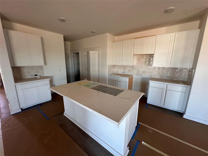 Kitchen with tasteful backsplash, white cabinetry, a center island, stovetop, and a textured ceiling Kitchen with tasteful backsplash, white cabinetry, a center island, stovetop, and a textured ceiling