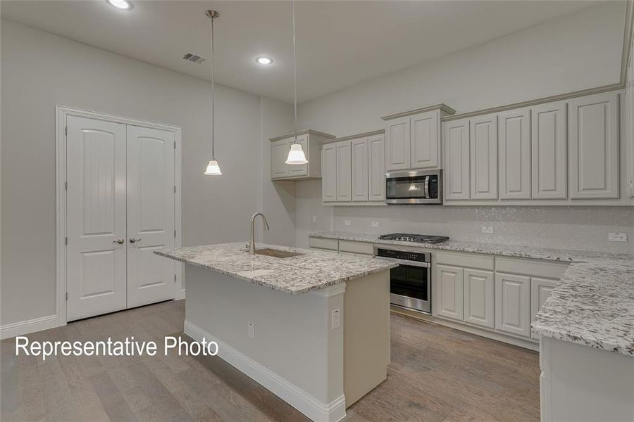 Kitchen with sink, stainless steel appliances, pendant lighting, light hardwood / wood-style flooring, and a center island with sink