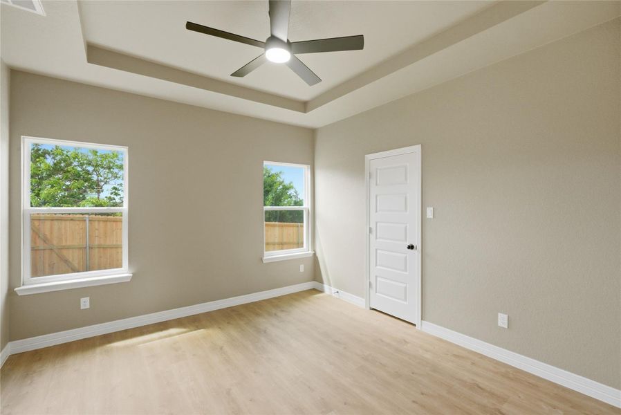 Empty room featuring light wood-style floors, ceiling fan, and a raised ceiling