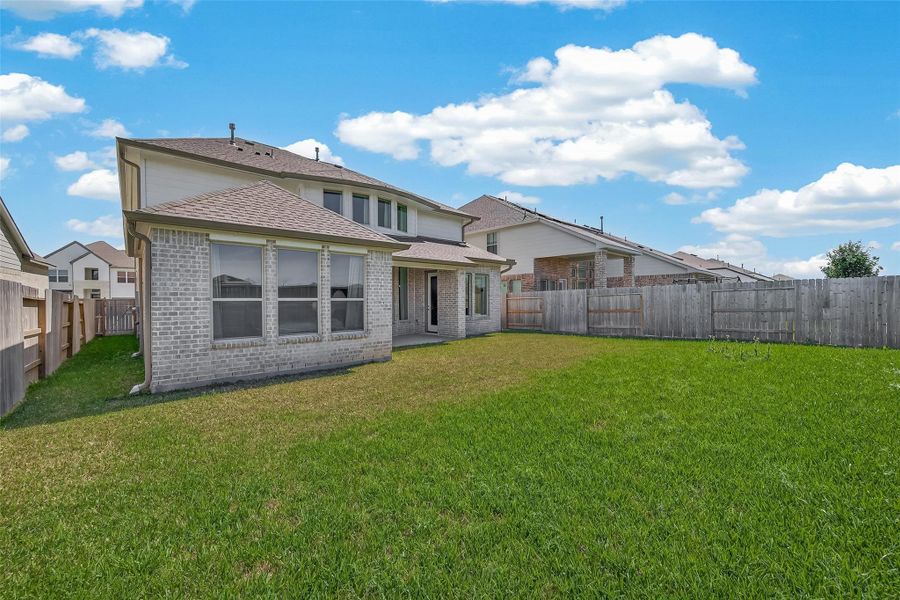 This photo showcases a spacious backyard with well-maintained grass, enclosed by a wooden fence. The back of the house features large windows and a covered patio area, ideal for outdoor relaxation.