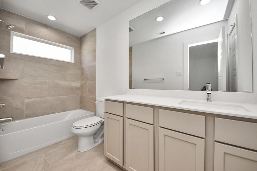 Secondary bath features tile flooring, bath/shower combo with tile surround, light stained wood cabinets, beautiful light countertop. Sample photo of completed home with similar floor plan. Actual colors and selections may vary.