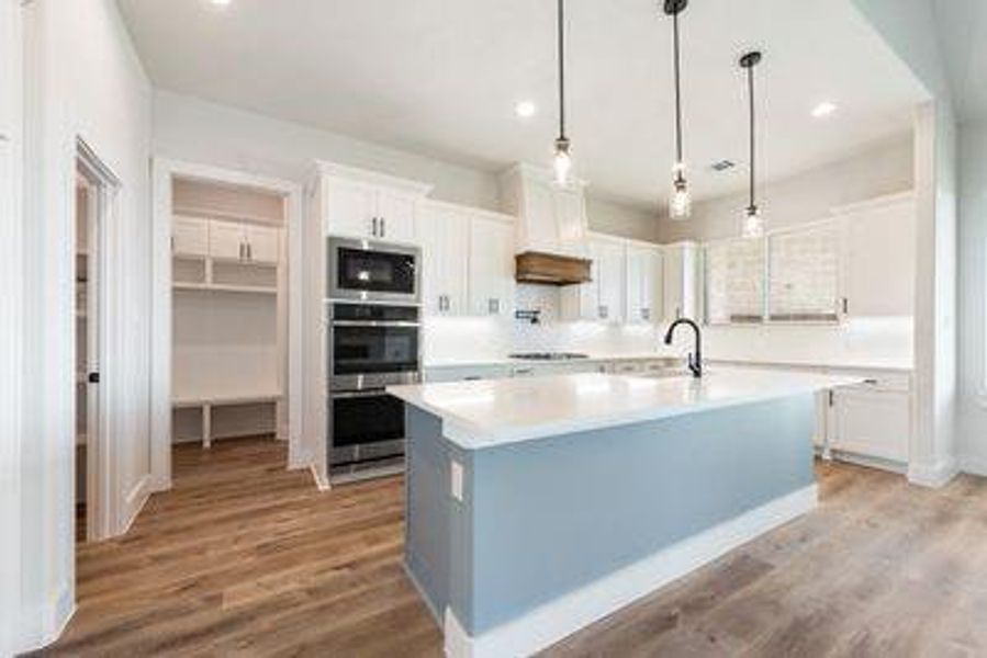 Kitchen featuring white cabinetry, stainless steel appliances, decorative light fixtures, light hardwood / wood-style flooring, and a kitchen island with sink