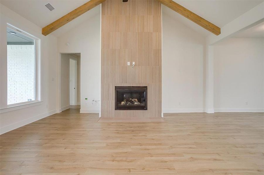 Unfurnished living room with light wood-type flooring, high vaulted ceiling, a tiled fireplace, and beamed ceiling