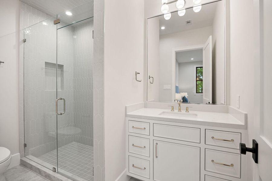 This stylish bathroom showcases a clean and modern aesthetic, with a spacious vanity and elegant finishes throughout. Bright lighting and a neutral palette enhance the airy feel. The highlight of this room is the glass-enclosed walk-in shower with beautifully tiled walls, creating a spa-like experience that blends luxury with everyday functionality.