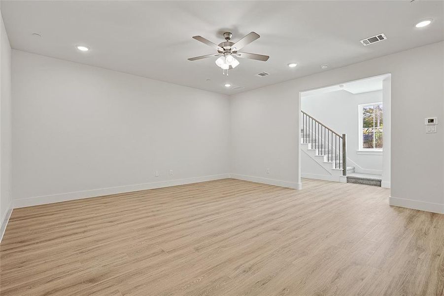 The expansive living area features light-toned flooring, recessed lighting, and a ceiling fan