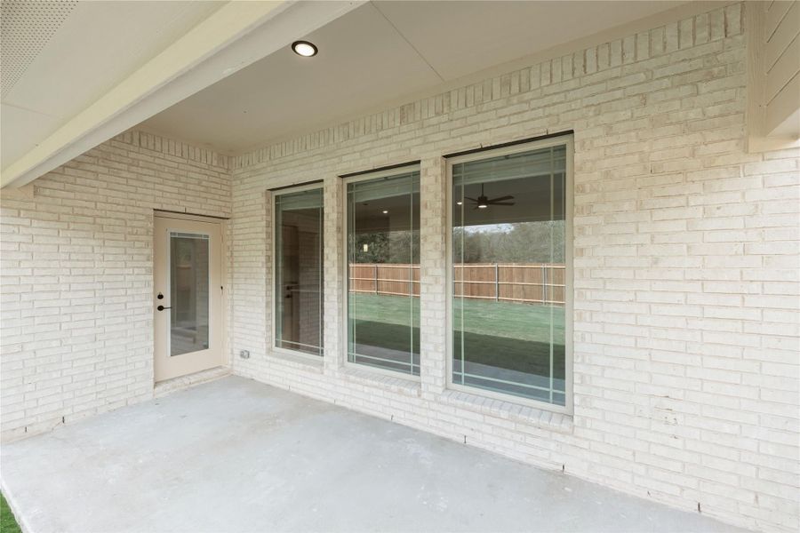 Covered concrete patio with white brick exterior, large windows, and glass back door overlooking fenced backyard