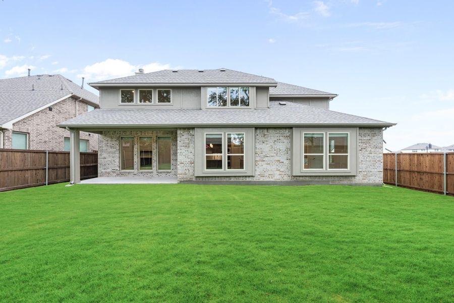 Two-story home rear exterior with brick facade, large windows, covered patio, and fenced green backyard Two-story home rear exterior with brick facade, large windows, covered patio, and fenced green backyard