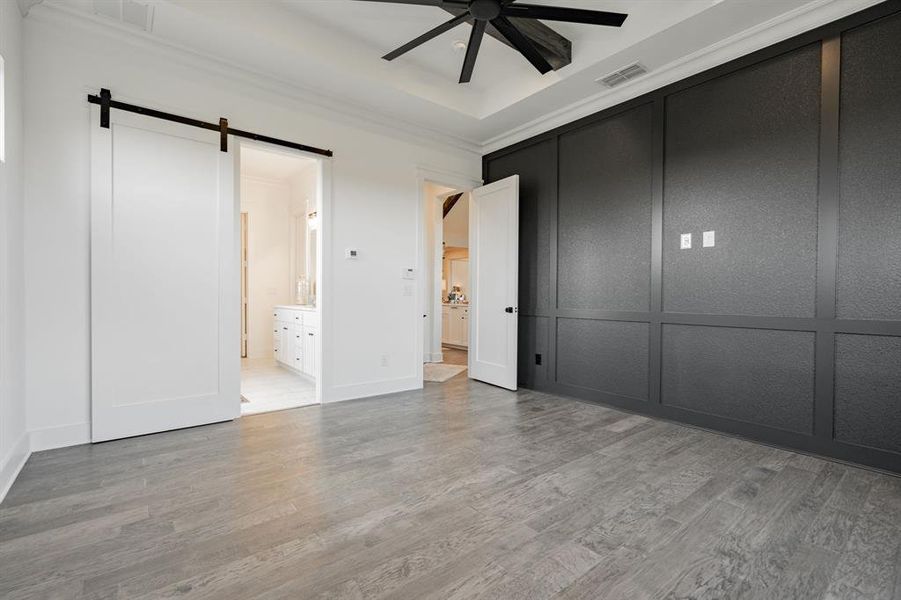 Unfurnished master bedroom with ceiling fan, ensuite bathroom, hardwood / wood-style floors, and a barn door